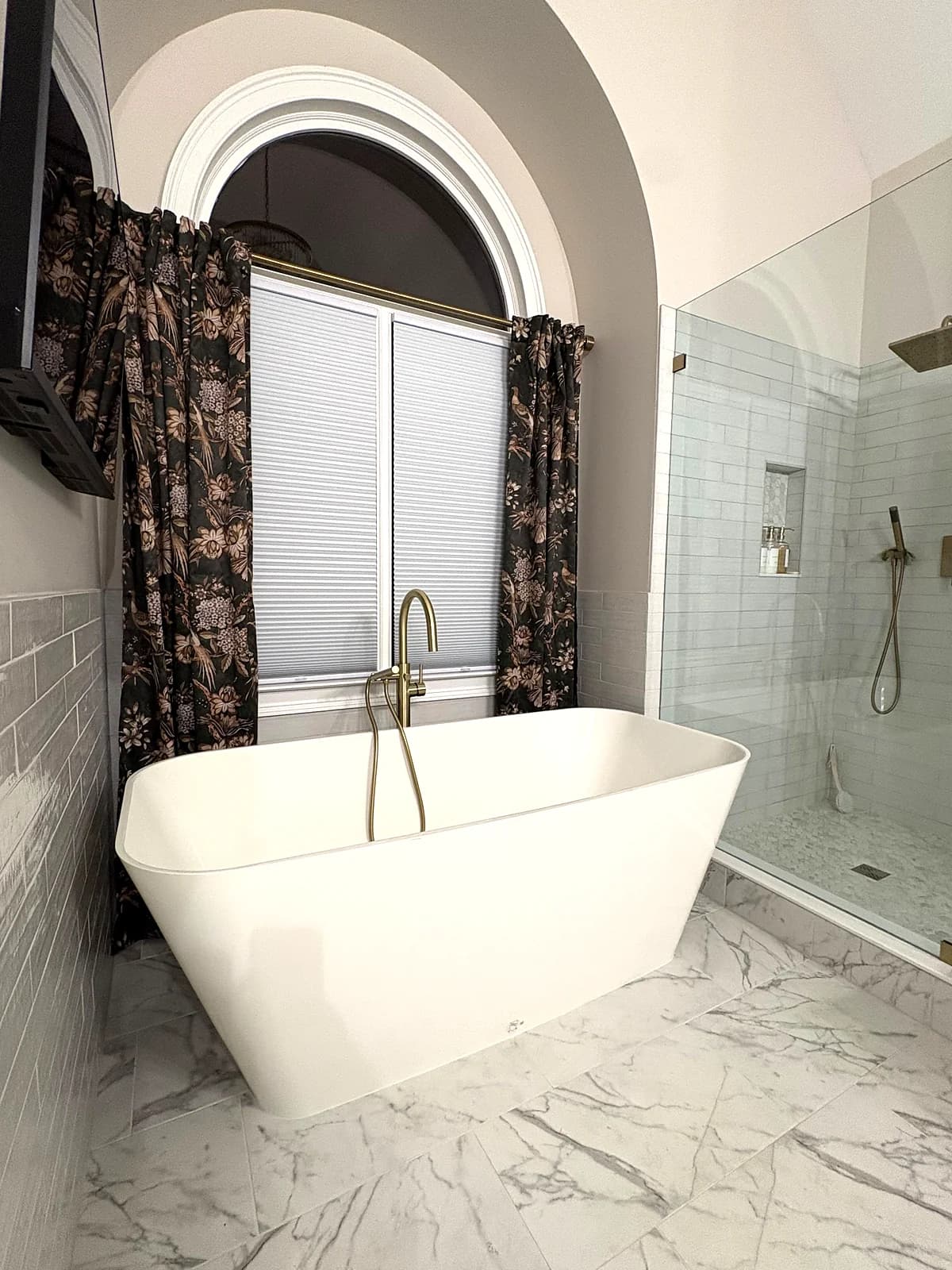 After: white freestanding tub with a floor-mounted faucet under the arched window, on marble-look porcelain floor tile