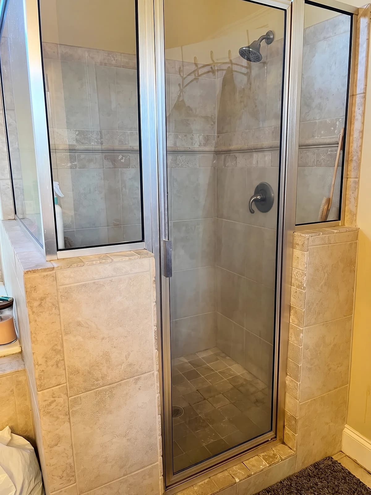 Before: corner shower with beige tile walls, a small tile floor, and an aluminum-framed glass door