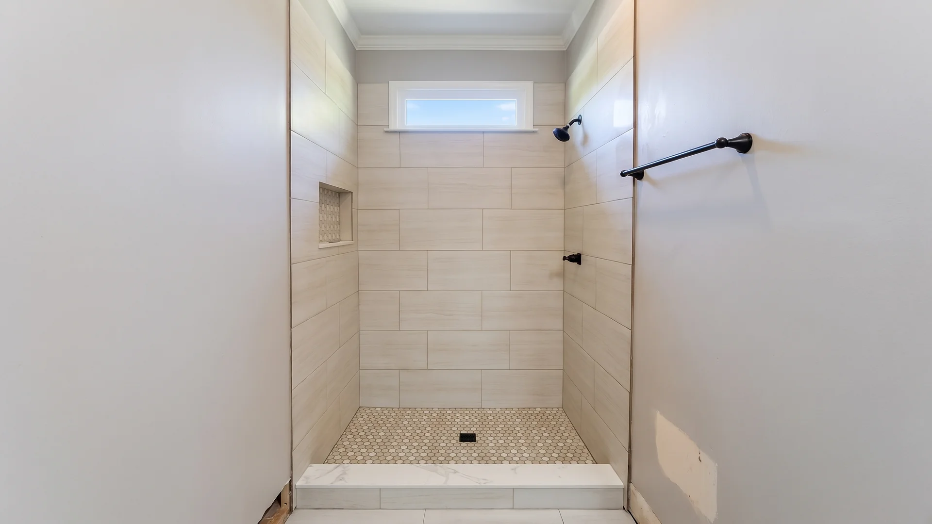 Beige subway tile walk-in shower with a recessed niche and mosaic floor