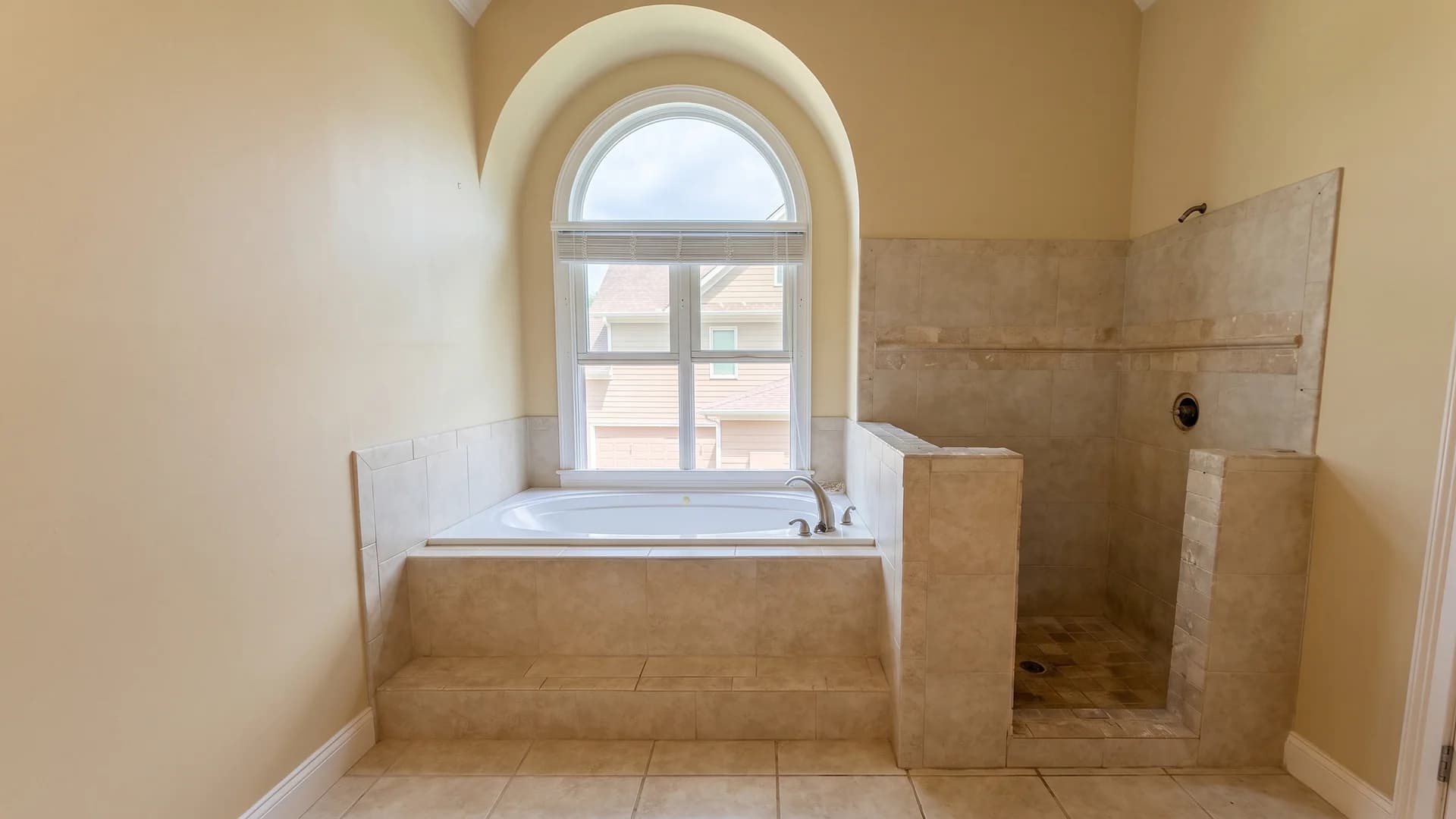 Remodeled bathroom with a beige tiled tub deck and walk-in shower under an arched window