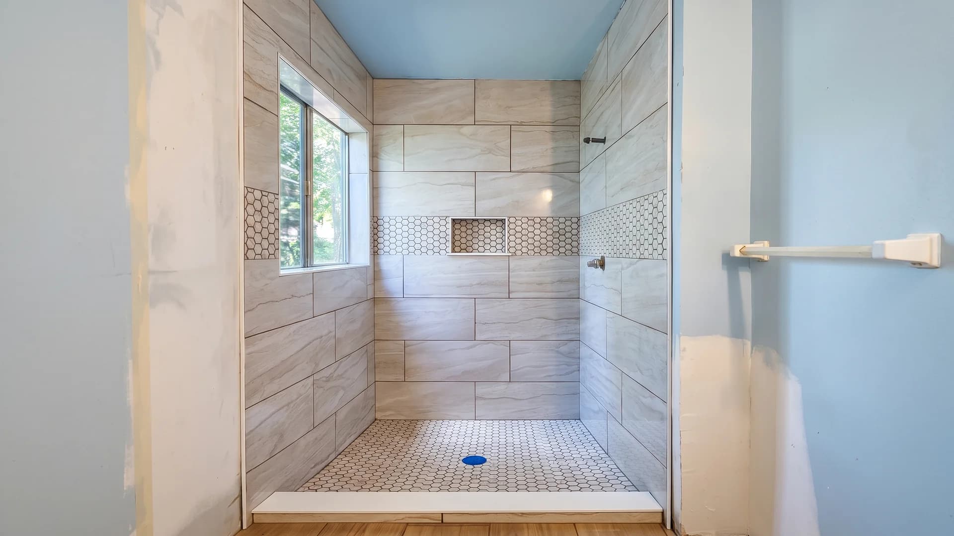 Walk-in shower with large-format wall tile, a mosaic niche band, and mosaic shower floor