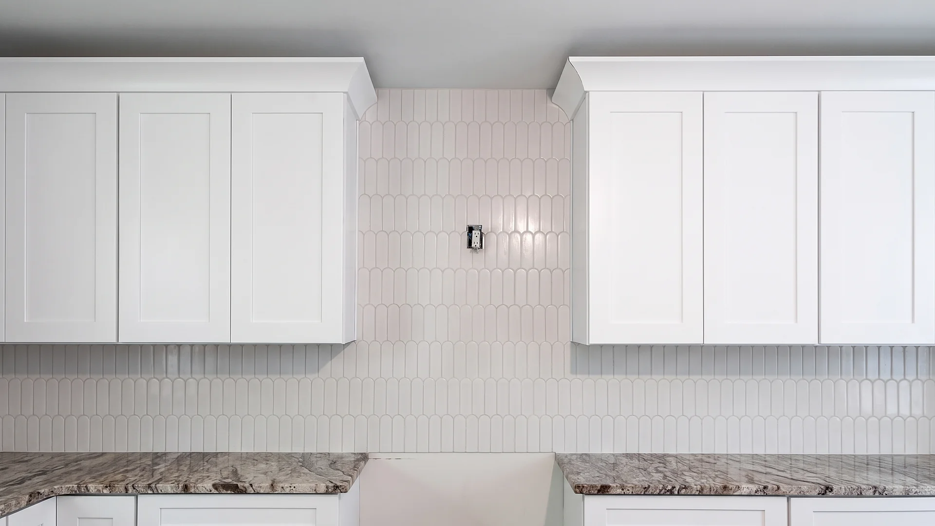 White arched tile kitchen backsplash between white upper cabinets