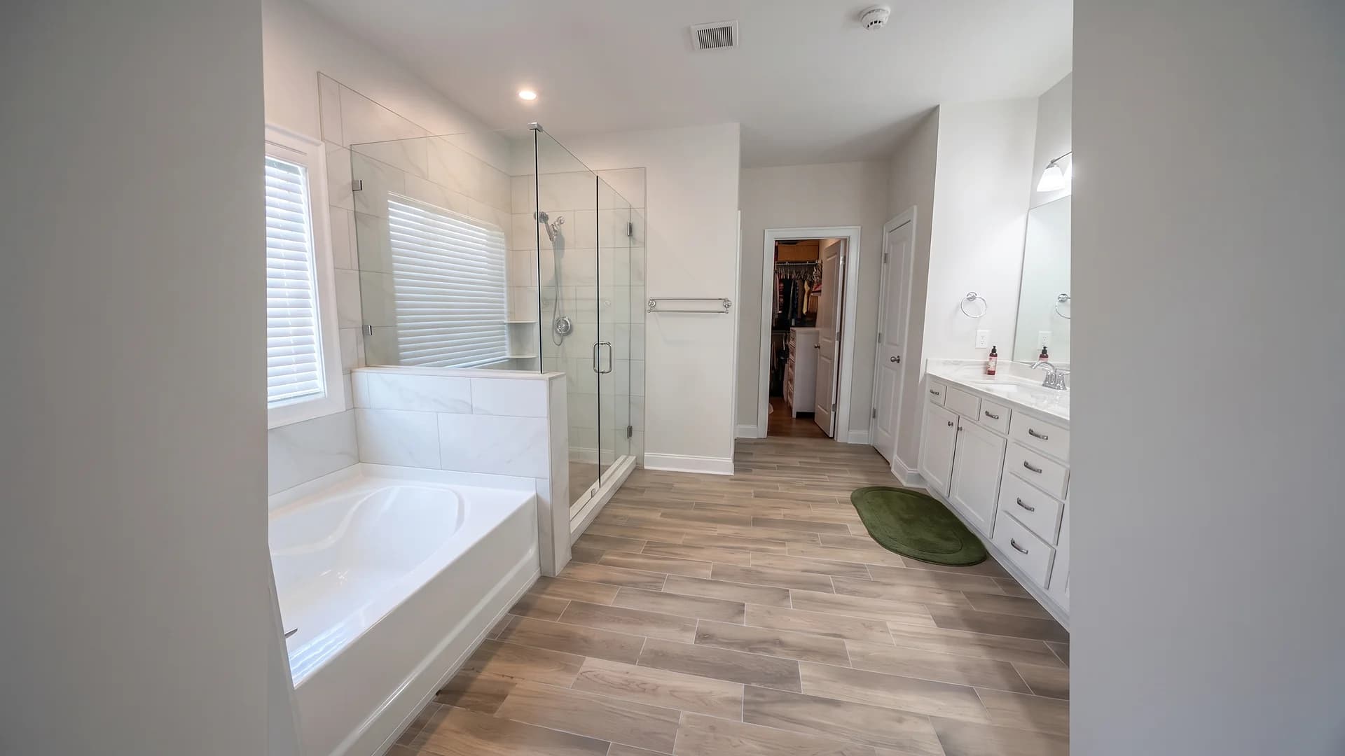 Wood-look plank tile floor installed through a bathroom with a soaking tub and glass shower